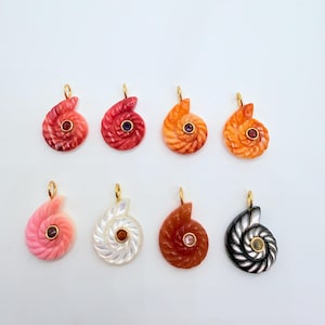 May include: Eight nautilus shell pendants in various colors, including red, orange, pink, white, brown, and black. Each pendant features a gold-colored bail and a central gemstone. The pendants are displayed against a white background.