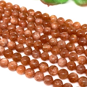 May include: A strand of round, orange sunstone beads. The beads are smooth and have a slightly translucent appearance.