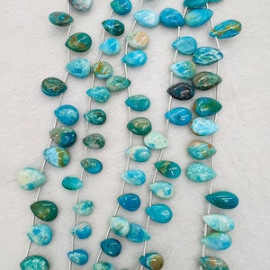 Op de afbeelding: Een streng turquoise edelsteen kralen in een druppelvorm. De kralen zijn een mix van licht en donkerblauw met bruine en witte marmering.