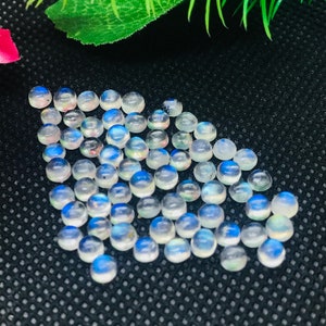May include: A collection of round, white moonstone cabochons with iridescent blue and rainbow flashes. The stones are approximately 6mm in diameter and are ideal for jewelry making.
