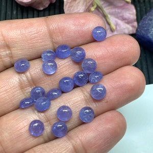 May include: A collection of round, light blue gemstones, likely amethyst or blue topaz, in various sizes. The gemstones are smooth and polished, with a slight sparkle.