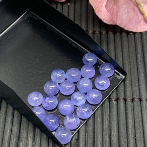 May include: A collection of round, smooth, light blue gemstones in a black tray. The gemstones are arranged in rows and are all approximately the same size.
