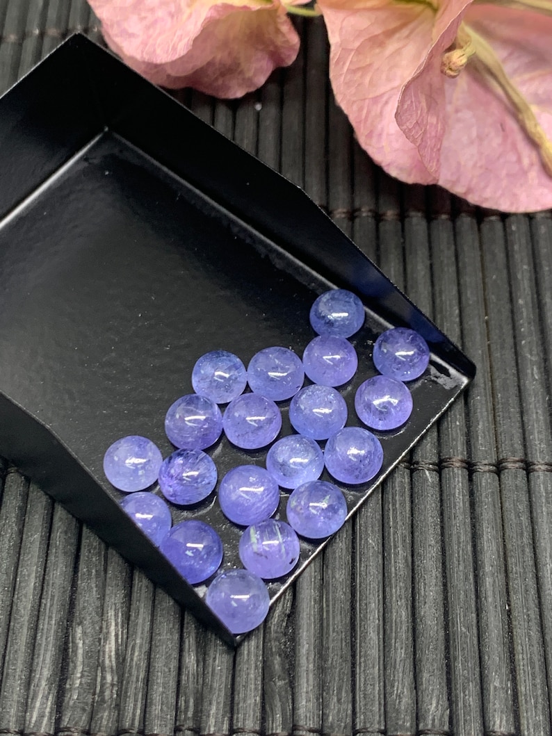 May include: A collection of round, smooth, light blue gemstones in a black tray. The gemstones are arranged in rows and are all approximately the same size.