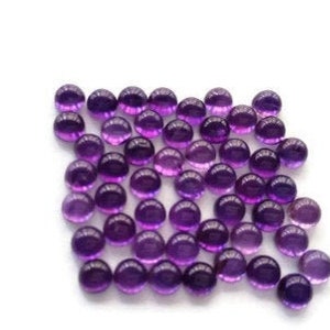 May include: A collection of round, purple amethyst cabochons. The cabochons are smooth and polished, with a slight sheen.