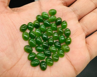 May include: A pile of 30 oval-shaped green jade stones, approximately 10mm in size, on a person's hand.