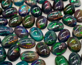 Puede incluir: Una colección de ópalos negros de forma ovalada con destellos iridiscentes verdes, azules y rojos. Los ópalos están sueltos y listos para ser engastados en joyas.