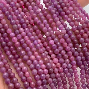 Op de afbeelding: Een streng paarse edelsteen kralen, elke kraal is rond en glad. De kralen zijn geregen op een dun draad en zijn gerangschikt in een nette rij.