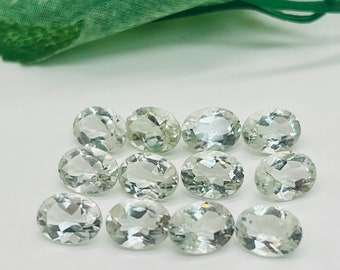 Puede incluir: Doce piedras preciosas ovaladas de color verde claro sobre un fondo blanco.