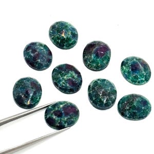 May include: A collection of oval-shaped gemstones with a faceted surface. The stones display a mix of deep green and burgundy colors. A pair of tweezers holds one of the gemstones, showcasing the intricate details and color variations.