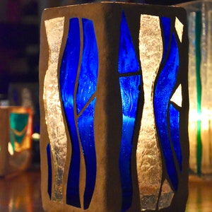May include: A square, gray, concrete candle holder with a blue and white stained glass design. The glass is in a wavy pattern.