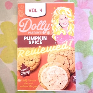 May include: A box of Dolly Parton's pumpkin spice cookies. The box features a photo of Dolly Parton and the text "VOL. 4 Dolly Parton's Pumpkin Spice Reviewed!" The cookies are soft and chewy.