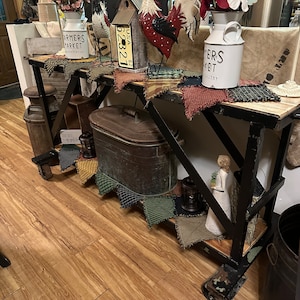 May include: A black metal console table with a wooden top. The table is decorated with a variety of farmhouse-style items, including a rooster figurine, a birdhouse, a vintage-style milk jug, and a variety of fabric scraps. The table is set on a wooden floor.