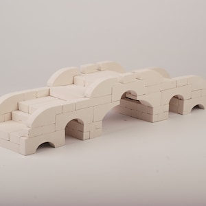 May include: A white toy bridge made of interlocking blocks. The bridge has three arches and a set of stairs leading up to the top.