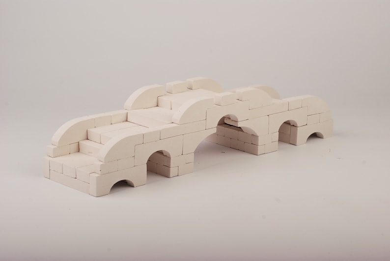 May include: A white toy bridge made of interlocking blocks. The bridge has three arches and a set of stairs leading up to the top.