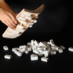 May include: A wooden tray with white tiles, being lifted up to reveal a pile of white tiles on a black surface.