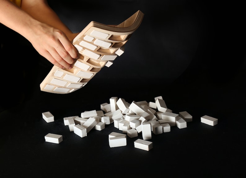 May include: A wooden tray with white tiles, being lifted up to reveal a pile of white tiles on a black surface.