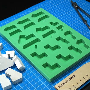May include: A green silicone mold with various geometric shapes, a set of white geometric shapes, a compass, and a wooden ruler with the text "PLANMAKEBUILD".