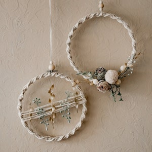 Könnte beinhalten: Zwei Makramee-Ringe mit floralen Akzenten. Der größere Ring hat eine Ansammlung von beige und rosa Blüten mit grünen Blättern. Der kleinere Ring hat ein gewebtes Design mit goldenen und grünen Akzenten.