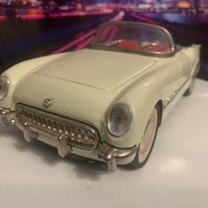 May include: Cream-colored vintage toy convertible car with red interior. The classic car has chrome accents, a detailed front grille, and white-walled tires. A collectible model car.