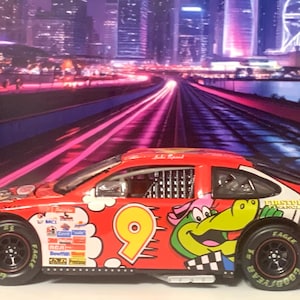 May include: A red toy race car with the number 9 on the side, featuring cartoon graphics of a crocodile and other characters. The car has black tires and is set against a cityscape background.