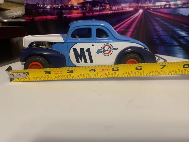 May include: A blue, white, and navy toy car with the number "M1" on the side. The car has red wheels and measures approximately 7 inches in length. The car has the words "Zip Italian Mille Miglia" on the side.