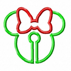 Puede incluir: Un diseño bordado en verde y rojo que representa un lazo y una forma de ojo de cerradura, que se asemeja a la cabeza de un personaje de dibujos animados. El lazo es rojo, y el contorno de la cabeza y el ojo de cerradura es verde, sobre un fondo blanco.