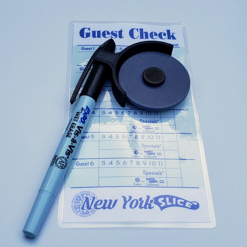 May include: A blue wet-erase marker labelled "Expo Vis-&agrave;-vis" is lying on top of a white paper guest check with the text "Guest Check" and "New York Slice". The guest check has a grid with numbers 1-11 and the word "Specials" repeated three times. A black and grey plastic pizza cutter is also on the paper.