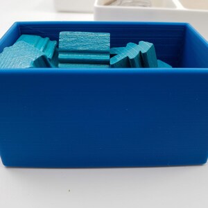 Puede incluir: Una caja de almacenamiento de pl&aacute;stico azul llena de piezas de madera de color turquesa. La caja est&aacute; vac&iacute;a, excepto por las piezas de madera.