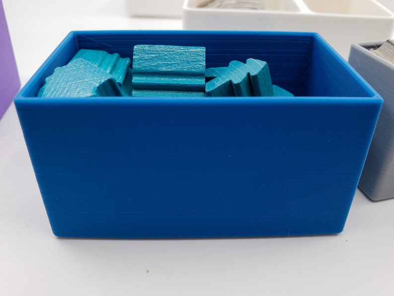 Puede incluir: Una caja de almacenamiento de pl&aacute;stico azul llena de piezas de madera de color turquesa. La caja est&aacute; vac&iacute;a, excepto por las piezas de madera.