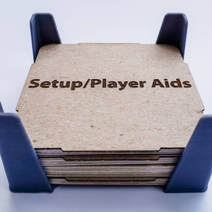 May include: A stack of cardboard player aid cards with the text "Setup/Player Aids" printed on the top card. The cards are held in a blue plastic frame.