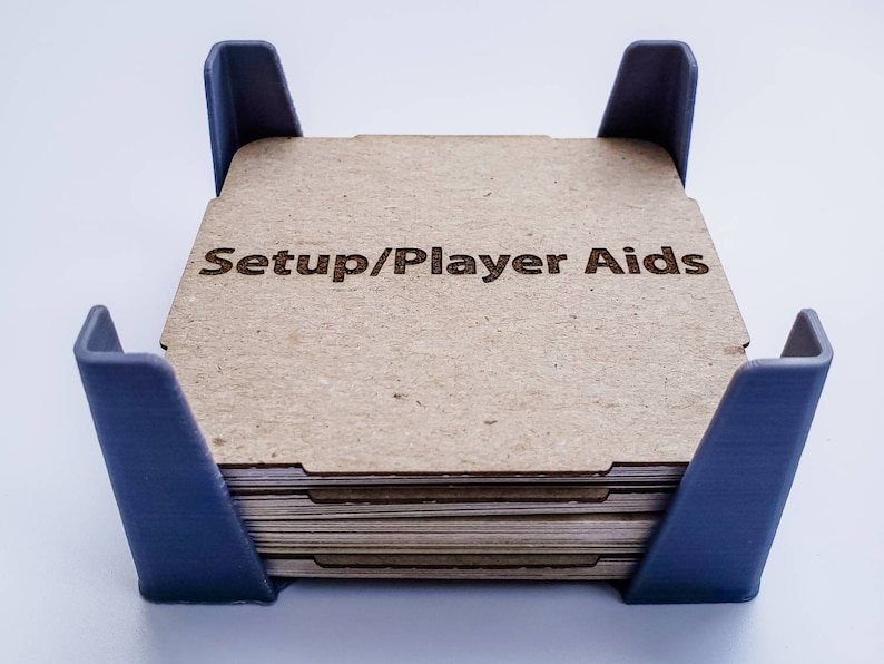 May include: A stack of cardboard player aid cards with the text "Setup/Player Aids" printed on the top card. The cards are held in a blue plastic frame.