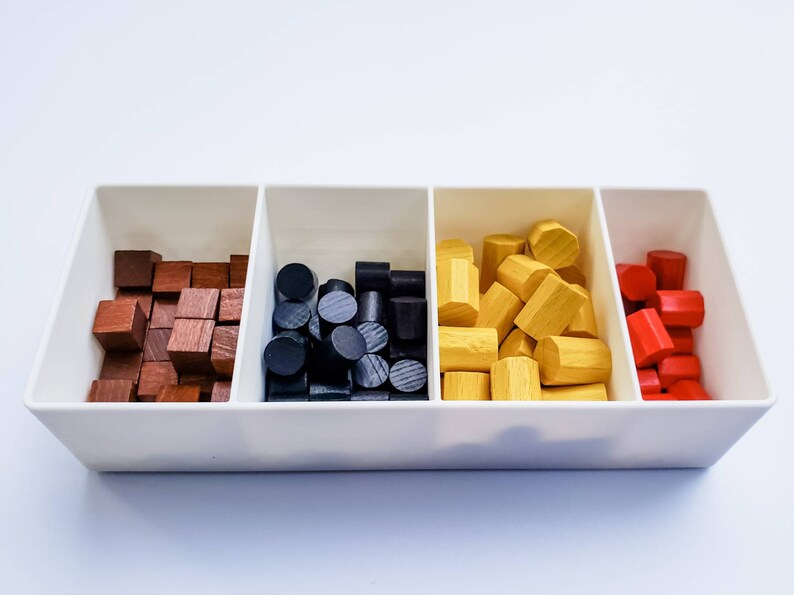 May include: A white tray with four compartments, each filled with wooden game pieces. The compartments contain brown, black, yellow, and red pieces.