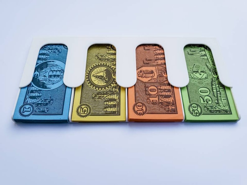 May include: Four Monopoly game money bills in a white plastic holder. The bills are blue, yellow, orange, and green. The bills are labelled with the amounts &pound;1, &pound;5, &pound;10, and &pound;50.