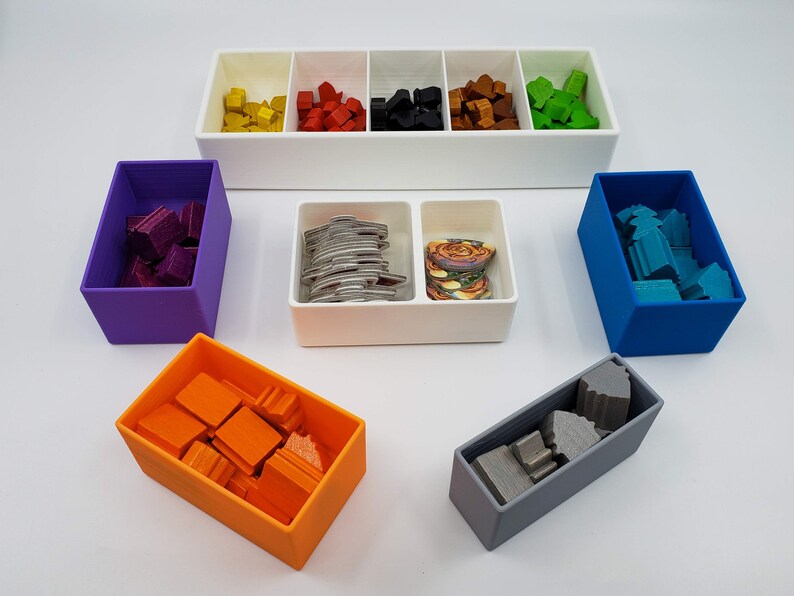 Puede incluir: Un conjunto de siete cajas de almacenamiento de colores con tapas, perfectas para organizar art&iacute;culos peque&ntilde;os. Las cajas son de pl&aacute;stico y vienen en una variedad de colores, incluyendo morado, naranja, azul, gris y blanco. Las cajas est&aacute;n llenas de varios art&iacute;culos peque&ntilde;os, como piezas de madera, fichas y cartas.