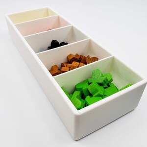 Puede incluir: Una caja rectangular blanca con cinco compartimentos. Los compartimentos est&aacute;n llenos de peque&ntilde;as piezas de madera de diferentes colores: verde, marr&oacute;n, negro, rojo y blanco.