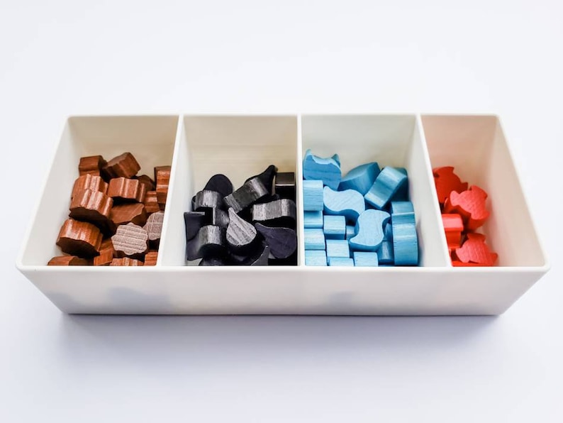 May include: A white tray with four compartments, each filled with wooden game pieces. The compartments contain brown, black, blue, and red pieces.