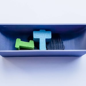 May include: A blue, green and black wooden tile set in a purple tray. The tiles are shaped like a cross, a letter L and a rectangle.