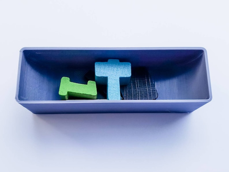 May include: A blue, green and black wooden tile set in a purple tray. The tiles are shaped like a cross, a letter L and a rectangle.