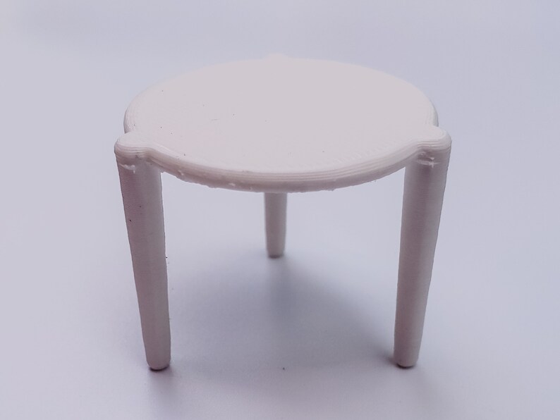 May include: A white, three-legged table with a round top. The table is made of plastic and is approximately 15 cm in diameter.