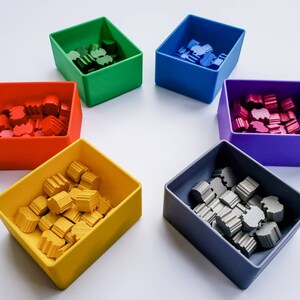 May include: Six small square containers, each filled with colourful wooden pieces. The containers are red, green, blue, purple, yellow, and grey.