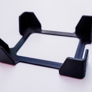 May include: A black plastic phone stand with four raised edges to hold a phone upright.