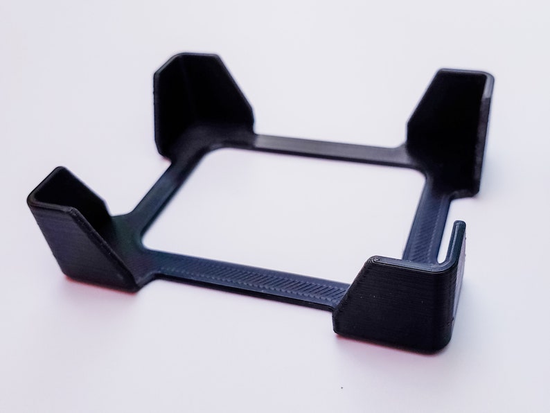 May include: A black plastic phone stand with four raised edges to hold a phone upright.