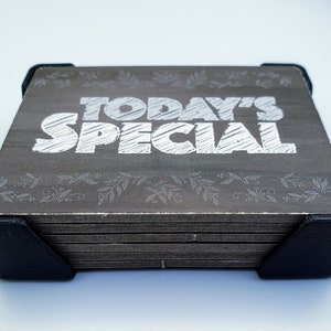 May include: A stack of wooden signs with a black frame. The top sign has a grey background with white text that reads "TODAY'S SPECIAL".
