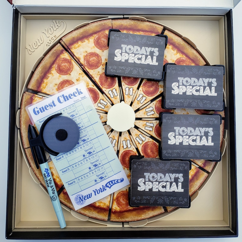 May include: A New York Slice pizza game board with a guest check, a pen, and four "Today's Special" cards. The board is made of cardboard and features a pizza with pepperoni slices.