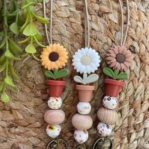 May include: Three floral keychains with brown, white, and yellow flower charms. Each keychain has a brown pot, a wooden bead, and a white bead with a floral pattern. The keychains are attached to gold metal key rings.