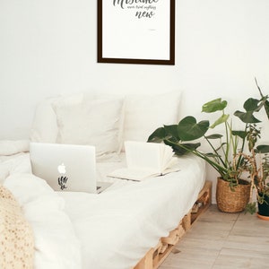 May include: A framed print with a white background and black text that reads "A person who never made a mistake never tried anything new." The print is hanging on a white wall above a bed with white bedding and a laptop computer on the bed.