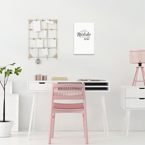 May include: A white desk with a pink chair, a white lamp with a pink shade, and a white wall with a black and white print that says "A little mistake can lead to something new".