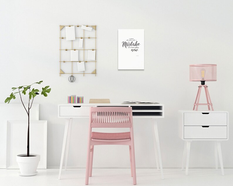 May include: A white desk with a pink chair, a white lamp with a pink shade, and a white wall with a black and white print that says "A little mistake can lead to something new".