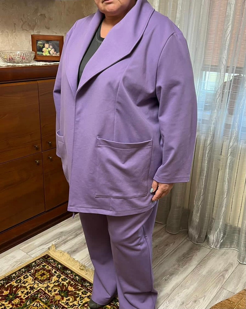 K&ouml;nnte beinhalten: Ein Lavendel-farbenes Hosenanzug mit einer lang&auml;rmeligen Jacke und einer weiten Hose. Die Jacke hat einen breiten Kragen und Taschen.