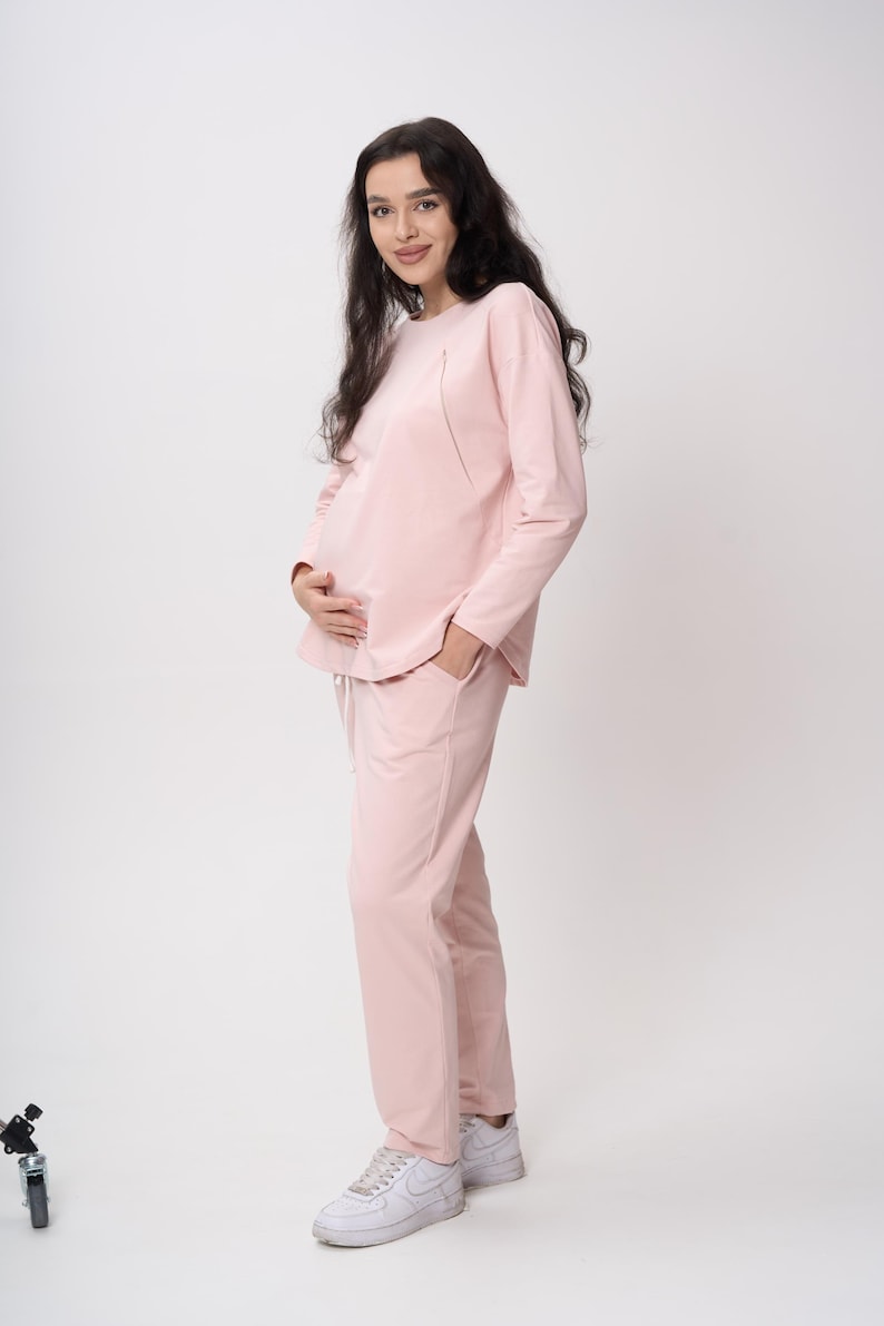 May include: A light pink long-sleeved top and matching long pants set. The top features a rounded neckline and long sleeves, while the pants have a drawstring waist and side pockets. The outfit is paired with white athletic sneakers.
